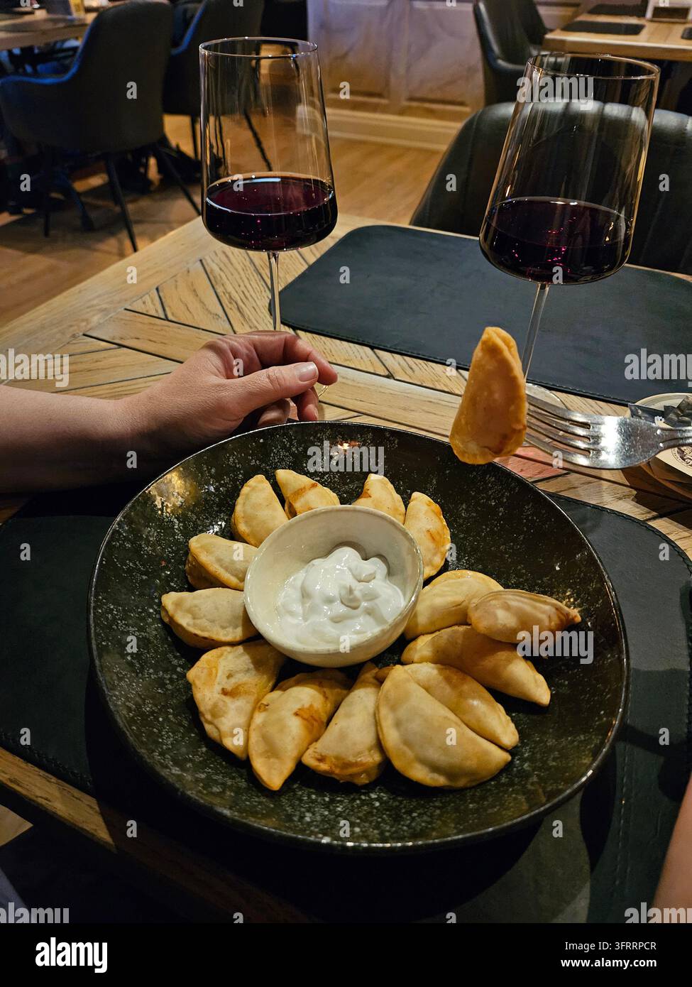 Un piatto di cibo con una ciotola di salsa bianca e due bicchieri di vino. La scena è rilassata e intima, mentre le persone stanno godendo insieme un pasto Foto Stock