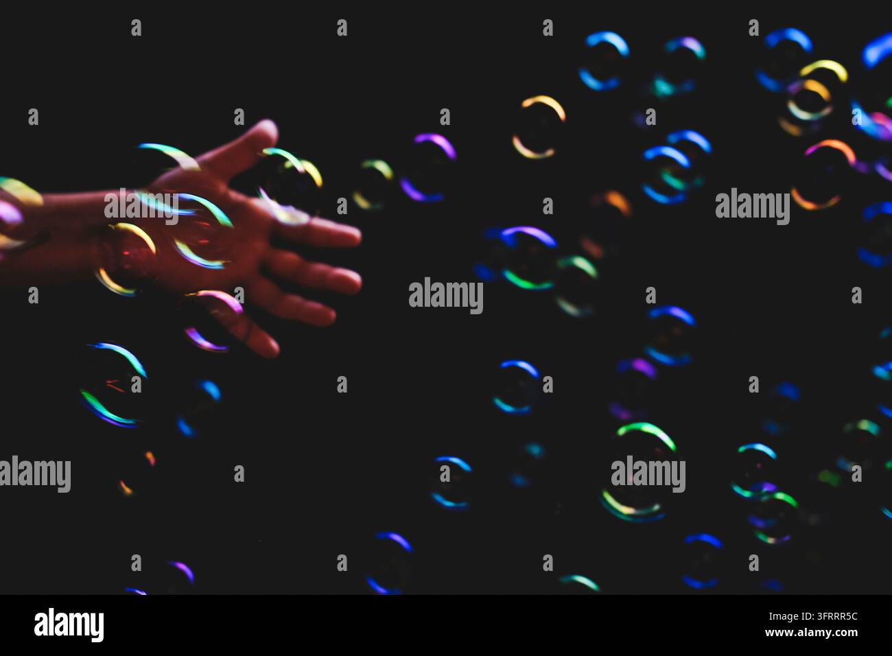 Bolle di sapone colorate volano su uno sfondo scuro e una mano umana cerca di catturarle Foto Stock