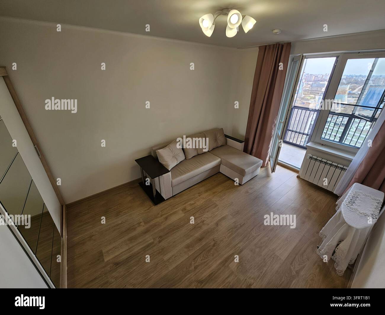 Soggiorno con divano e tavolino. Il divano è marrone e il tavolino è marrone. Tavolo da stiro in lino e balcone con vista sulla centrale elettrica (PR) Foto Stock