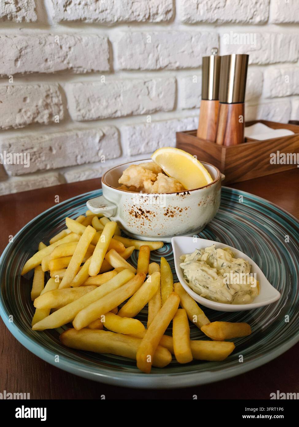 Piatto di patatine fritte e una ciotola di pesce impanato con un limone sopra. C'è anche una piccola ciotola di salsa sul piatto Foto Stock