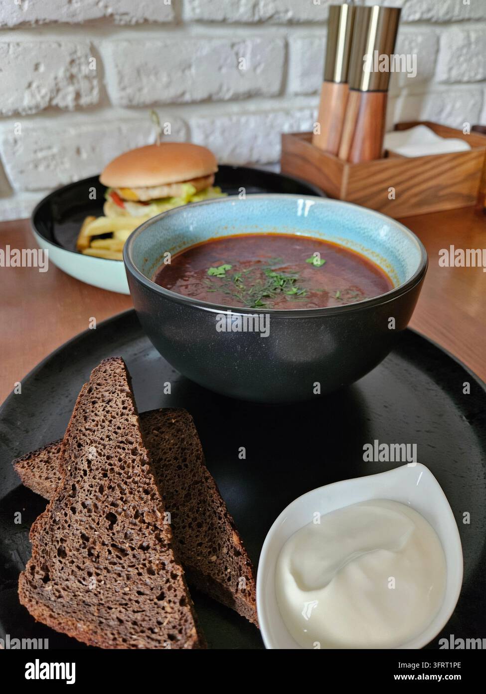 Piatto con un panino e una ciotola di zuppa borsch è posizionato su un tavolo. C'è anche una ciotola di salsa bianca accanto alla zuppa Foto Stock