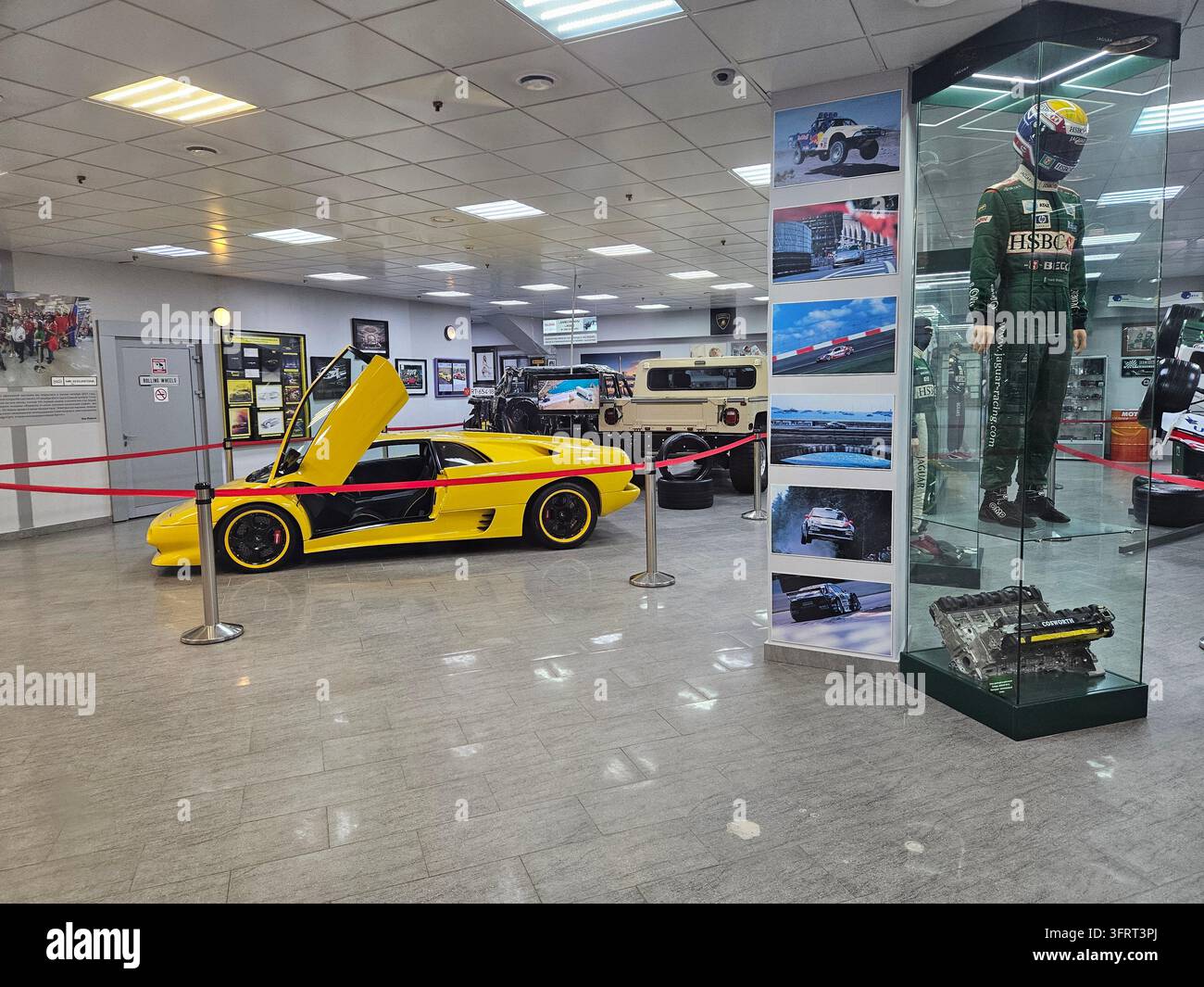 SOCHI - 16 MAGGIO 2025: Auto gialla con il cofano aperto è esposta nel museo Sirius Circuit. Un uomo in tuta da corsa verde è in piedi accanto all'auto Foto Stock