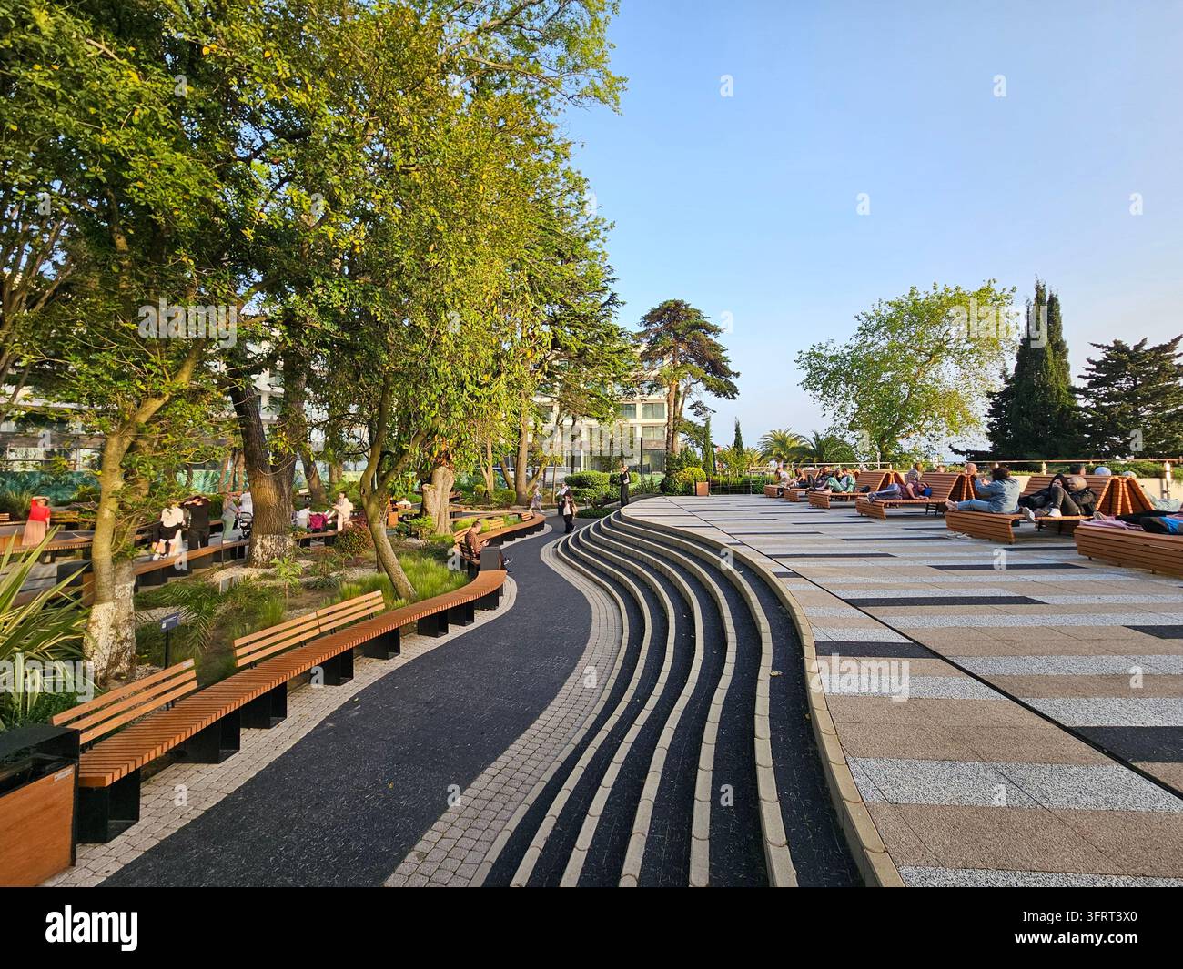 SOCHI - 16 MAGGIO 2025: Parco con un vialetto in pietra e panchine. Le persone sono sedute sulle panchine. Ci sono anche alcune piante in vaso Foto Stock