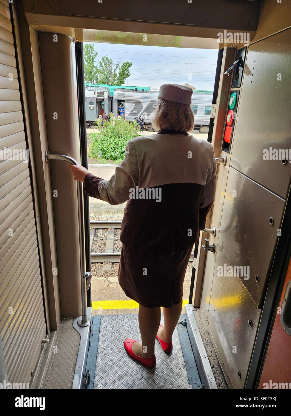 SOCHI - 19 MAGGIO 2025: Donna con cappello e uniforme in piedi davanti alla porta di un treno. Tiene una maniglia Foto Stock