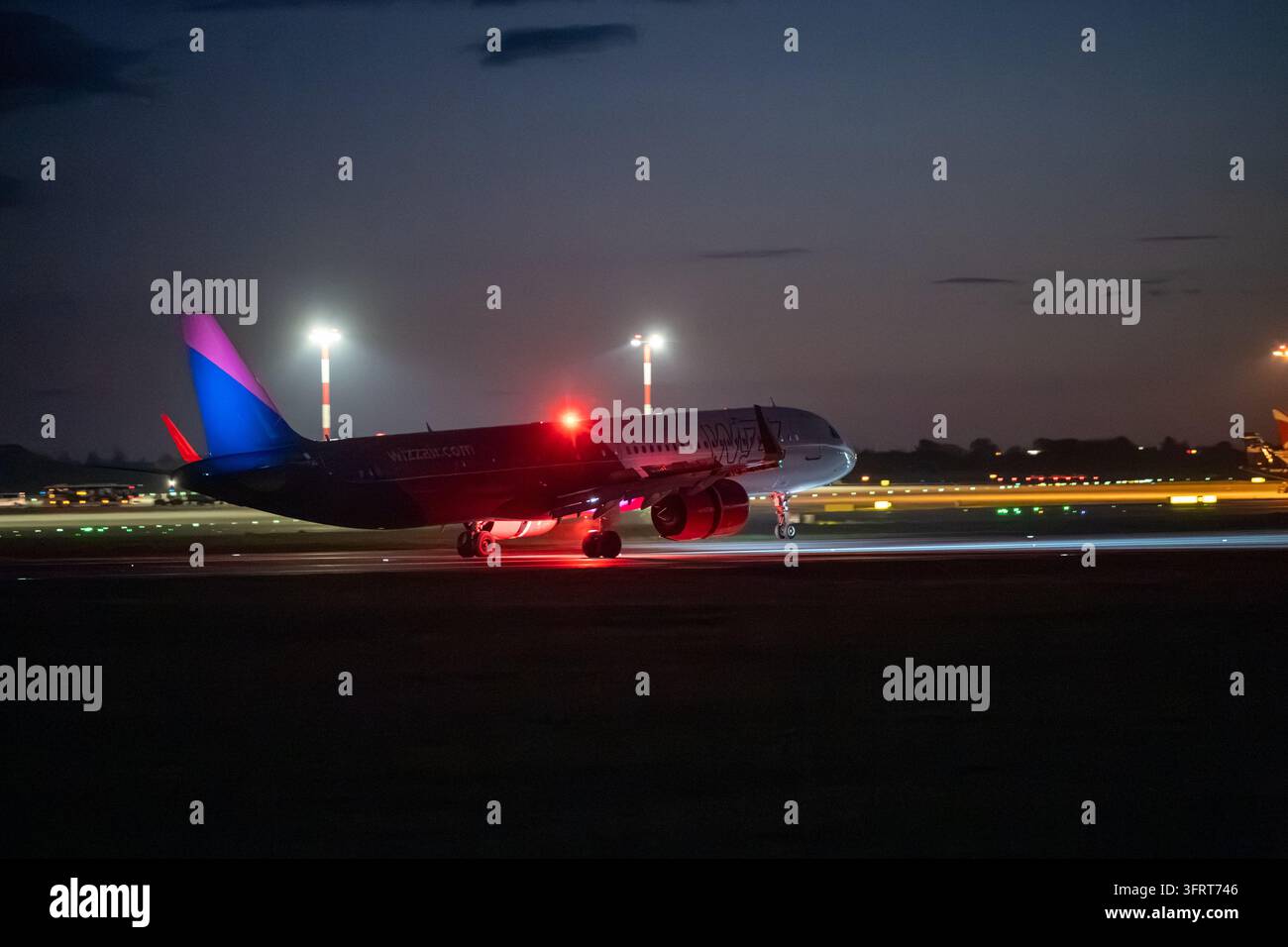 Airbus della Wizz Air che atterra al crepuscolo con il carrello di prua sollevato, le ruote principali sulla pista e il faro anti-collisione rosso che lampeggia. Praga, Repubblica Ceca Foto Stock