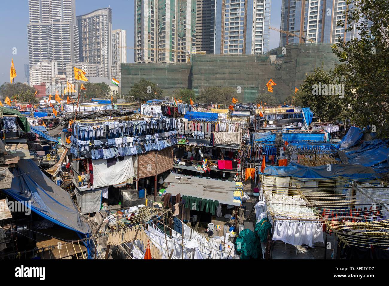 Vista aerea della lavanderia all'aperto di Dhobi Ghat con jeans lavati che asciughano sotto bandiere e grattacieli di lusso che si ergono dietro le capanne di lavaggio, Mumbai, India Foto Stock