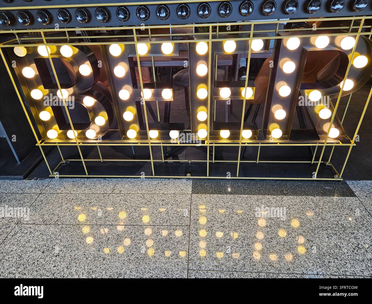 Insegna grande con la parola birra scritta in luci al neon. L'insegna è circondata da una cornice metallica ed è illuminata, creando una presentazione luminosa e accattivante. La scena è energica e invitante Foto Stock