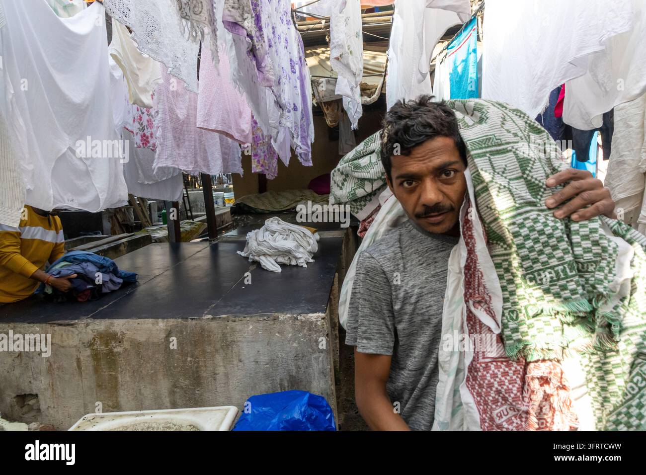 Ritratto di un uomo con i baffi che porta un asciugamano a quadri verdi e rossi sulle spalle davanti al bucato a Dhobi Ghat, Mumbai, India Foto Stock