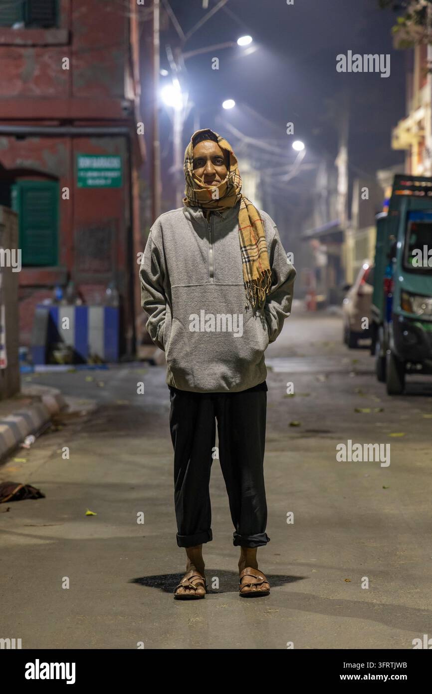 Ritratto di un uomo con le mani in tasca e sandali in piedi su una strada tranquilla fiancheggiata da vecchi edifici in mattoni e camion parcheggiati sotto i lampioni, West Be Foto Stock