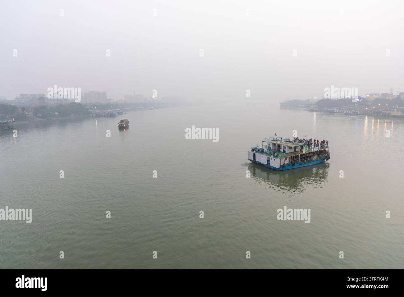 Barca a due piani trasporta pendolari su acque grigie e calme mentre un'altra imbarcazione e i contorni sfumati degli edifici si perdono nella nebbia, Bengala Occidentale, Kolkata Foto Stock