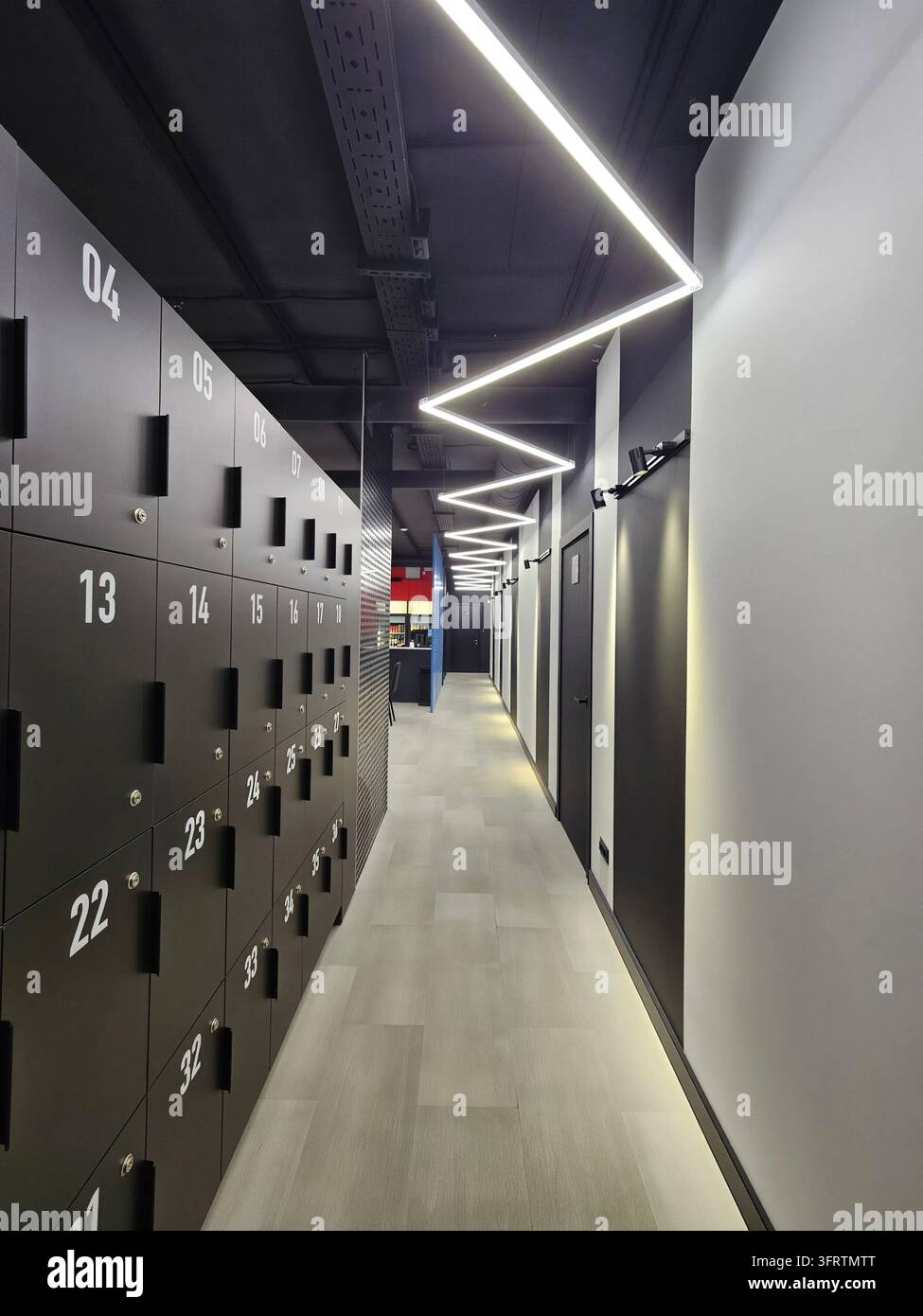 Corridoio moderno con eleganti armadietti neri e illuminazione a LED. Design pulito e minimalista con pavimentazione grigio chiaro. Lungo corridoio che si estende in lontananza con armadietti ripetuti Foto Stock
