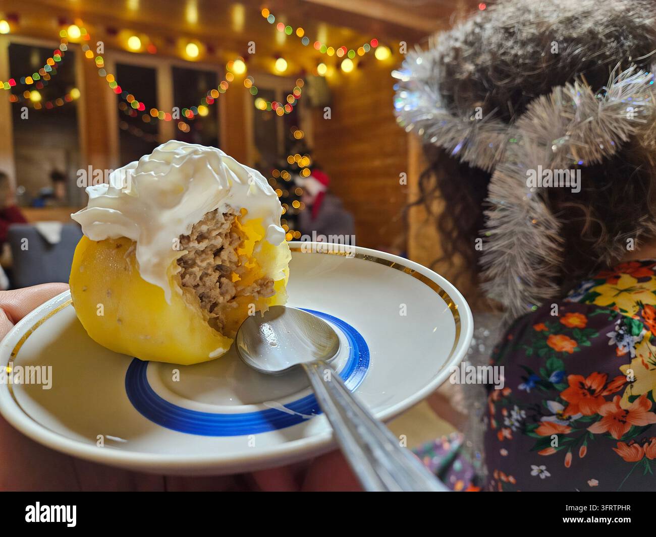 Ambientazione interna accogliente con luci calde a filo. Dumpling giallo ripieno di carne saporita e panna. Bambino con cappotto a fiori e cappello di pelliccia tiene un piatto. Parlato su uno sfondo festivo illuminato dolcemente Foto Stock