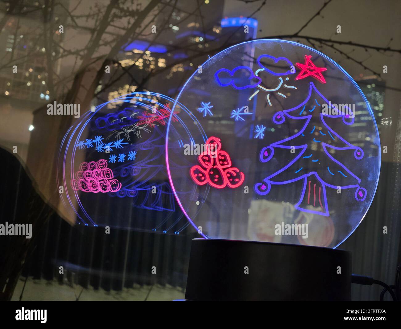 Sfere di vetro trasparente mostrano disegni natalizi luminosi. Luci al neon formano alberi di Natale e fiocchi di neve. Tonalità blu e viola illuminano forme festive. Accenti rossi e rosa evidenziano simboli gioiosi Foto Stock