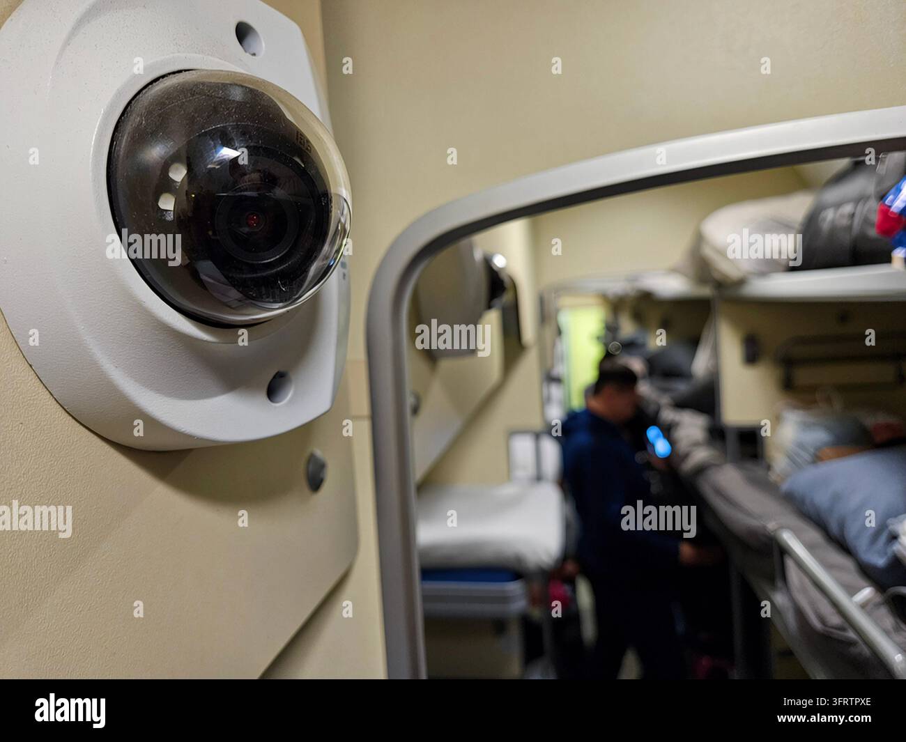 Telecamera di sicurezza montata all'interno del compartimento del treno. Persona visibile sullo sfondo sfocato. Letto a castello e bagagli mostrati in messa a fuoco morbida. L'obiettivo della telecamera riflette l'interno circostante Foto Stock