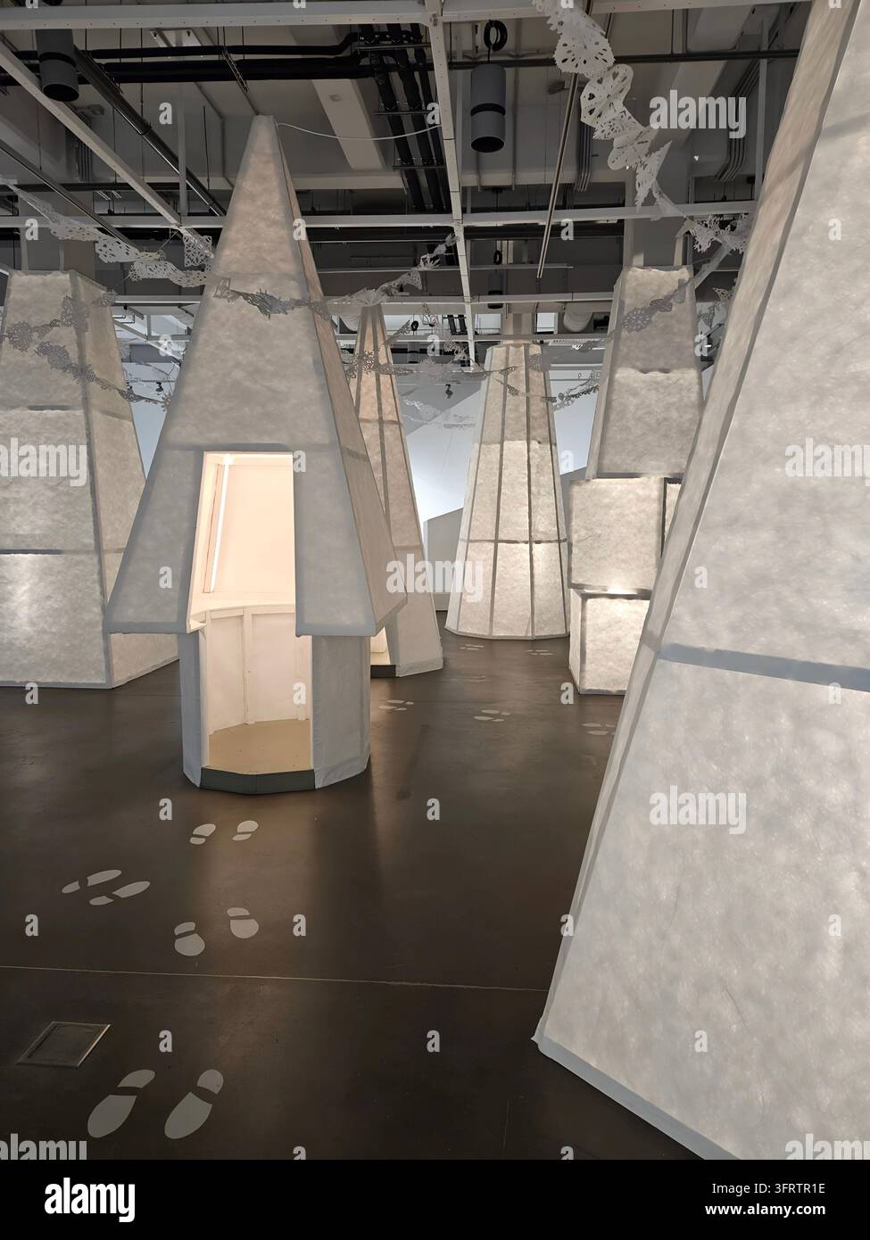 SAMARA - 13 GEN 2026: Installazione astratta con forme scultoree angolari e bianche. Pavimento in cemento con impronte di piedi sparse. Soffitto scuro con condotti e apparecchi di illuminazione visibili Foto Stock