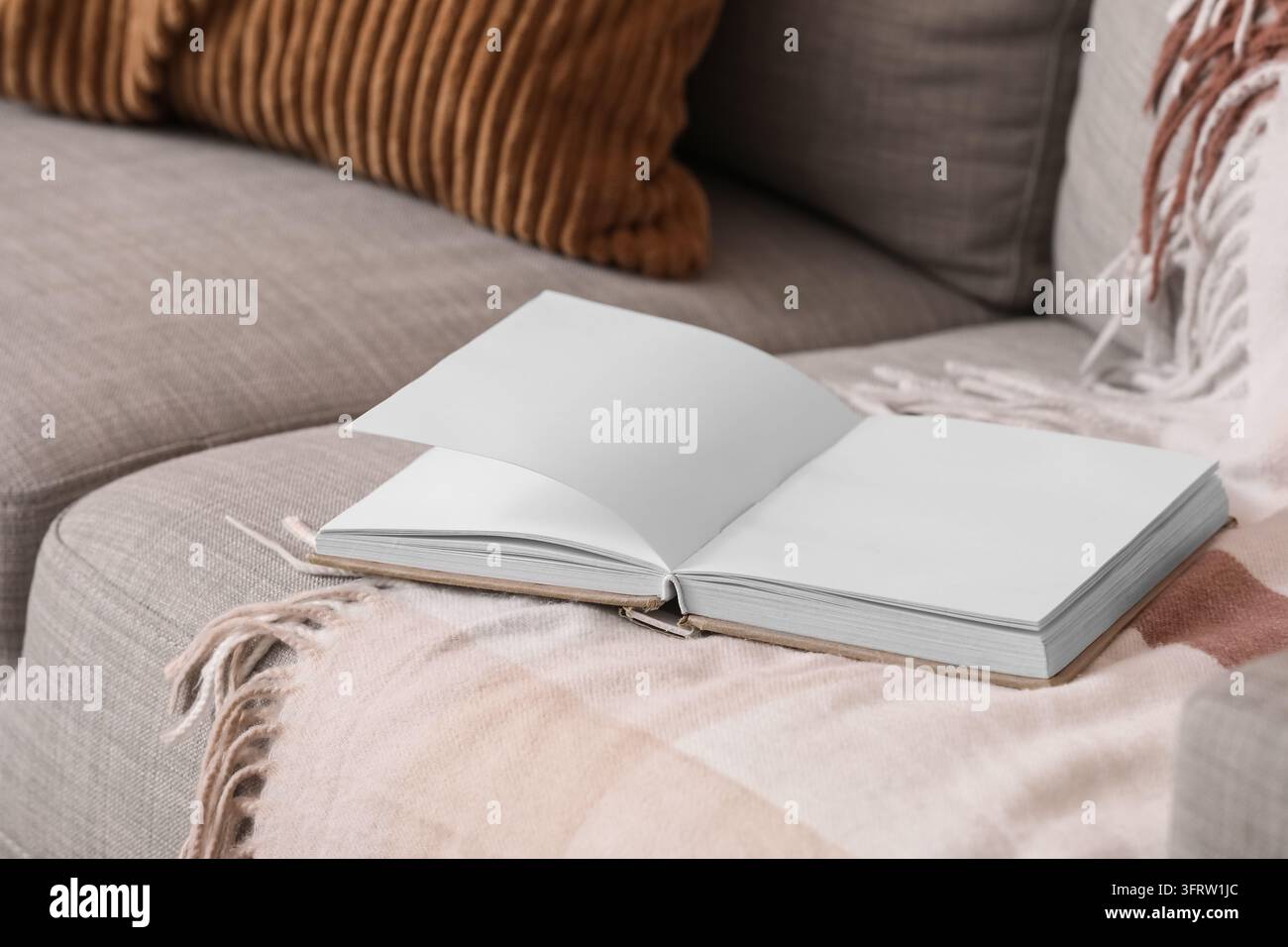 Concetto di consapevolezza e relax, quaderno vuoto aperto su un comodo divano con coperta morbida per il journaling o la scrittura creativa in un interno domestico Foto Stock