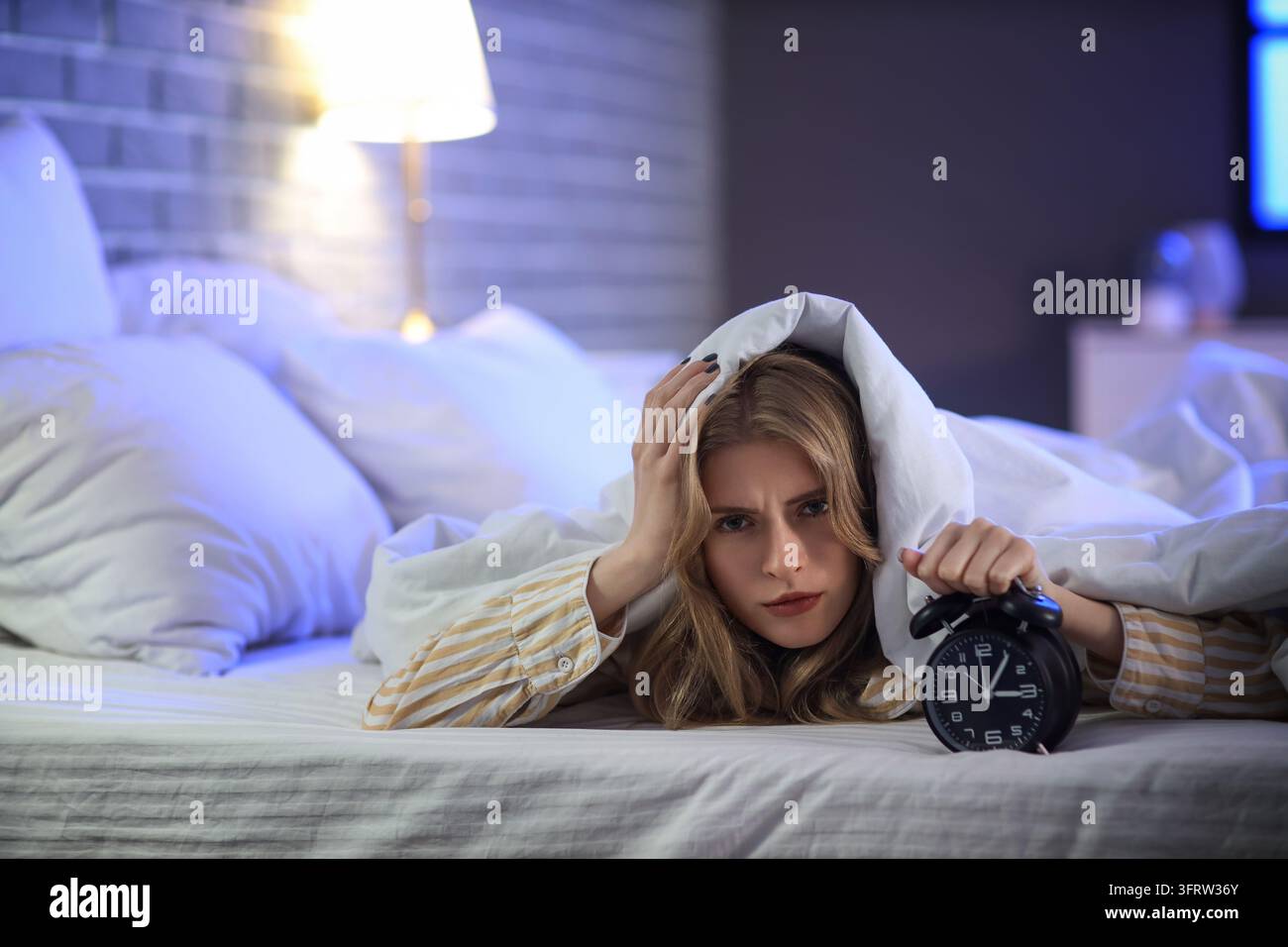 Insonnia e privazione del sonno, donna stressata sdraiata a letto di notte con sveglia che si sente esausta e stanca per la mancanza di riposo e l'ansia Foto Stock