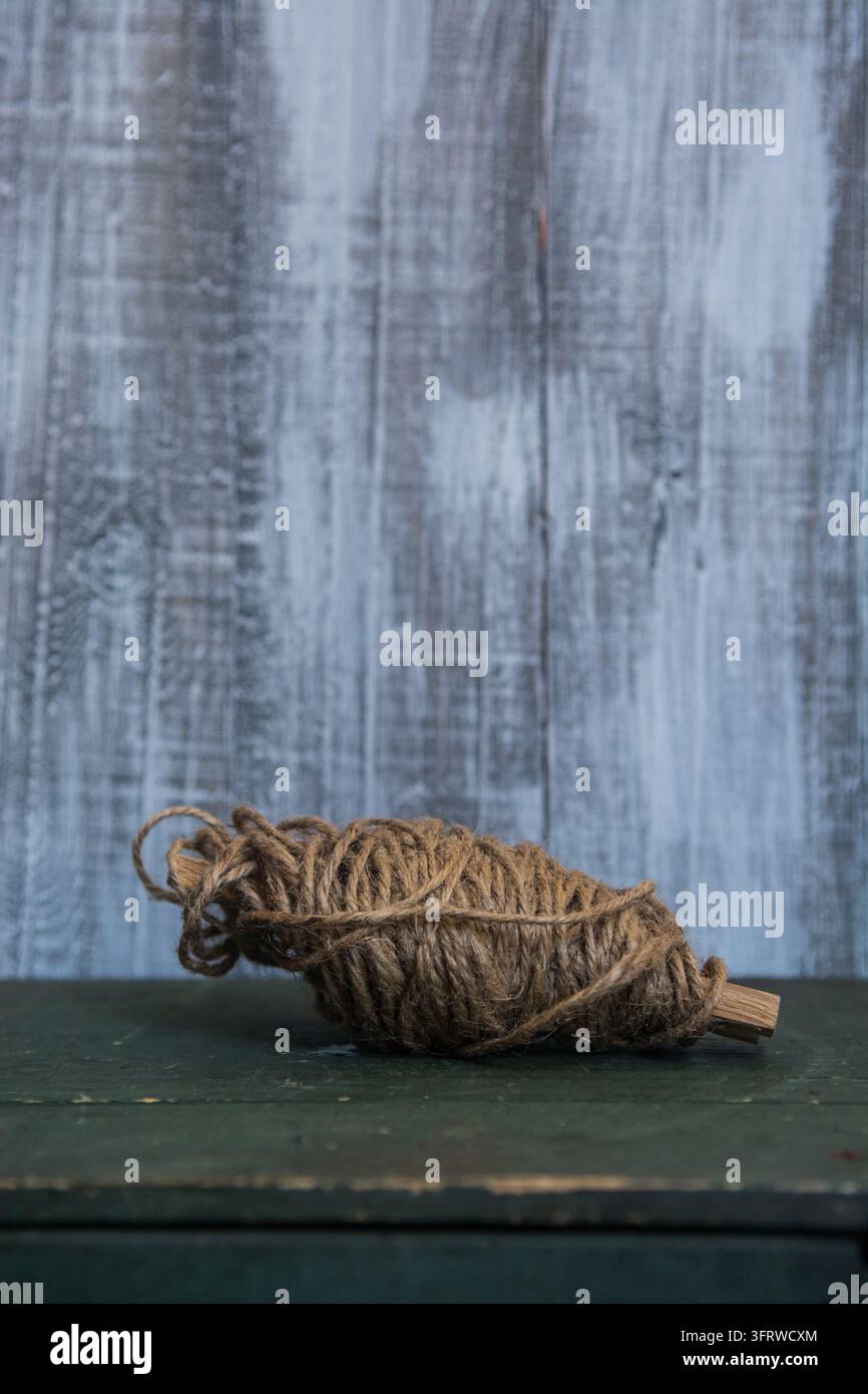 Una bobina ruvida di corda marrone poggia su un tavolo verde scuro contro un muro di legno blu consumato. Foto Stock