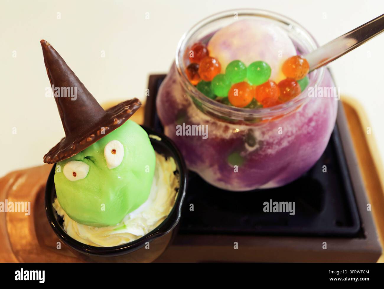 Gelato verde da strega carino per Halloween con sfondo sfocato di cocktail spaventoso in una pentola magica Foto Stock