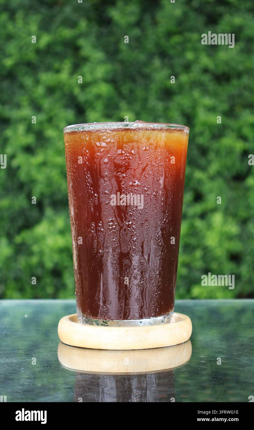 Un delizioso caffè freddo americano su un sottobicchiere, sfondo naturale rinfrescante con foglie verdi sfocate Foto Stock