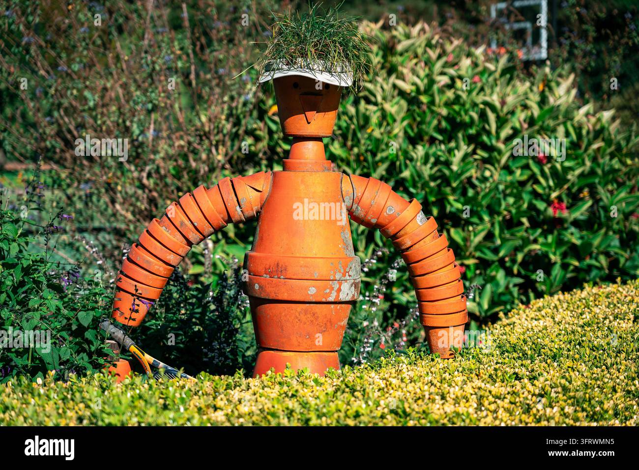 Figura di spaventapasseri in vaso di terracotta in un giardino verdeggiante Foto Stock