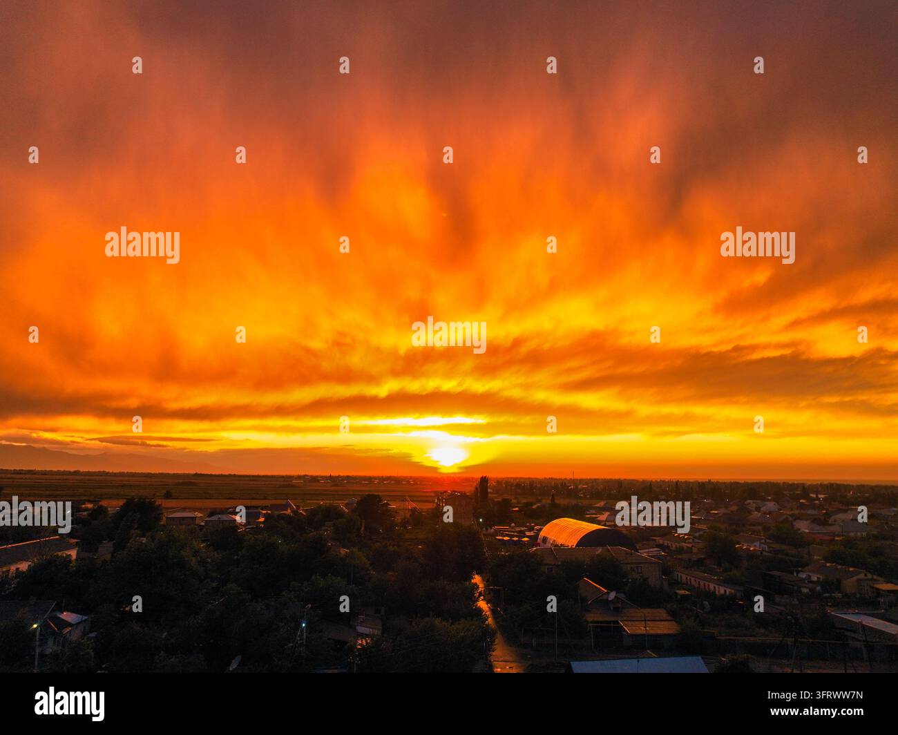 Tramonto infuocato arancione e giallo che brucia tra le nuvole tempestose sopra l'orizzonte della città Foto Stock