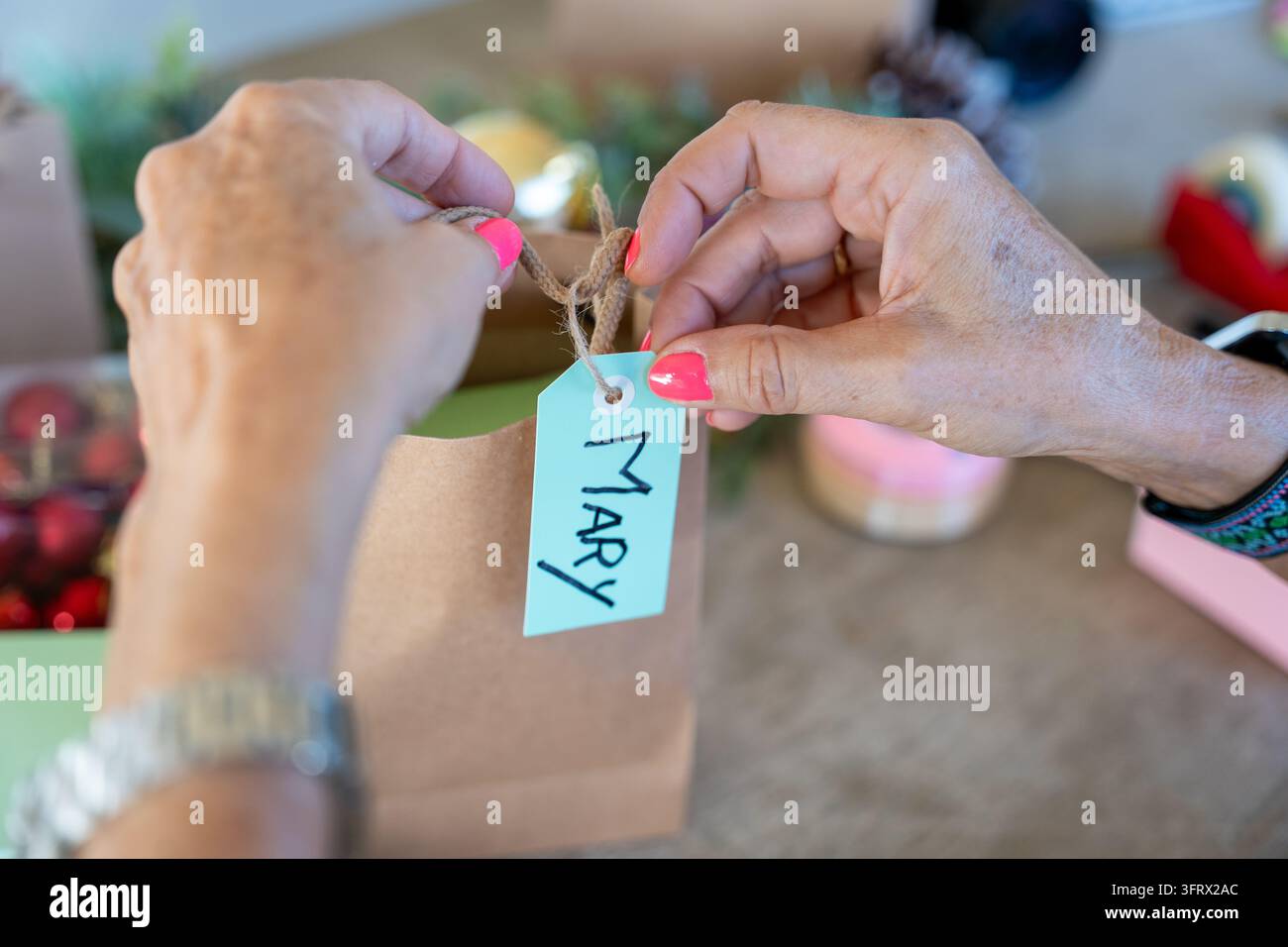 Mani di una donna che preparano una borsa regalo con un'etichetta personalizzata per una festa festiva Foto Stock