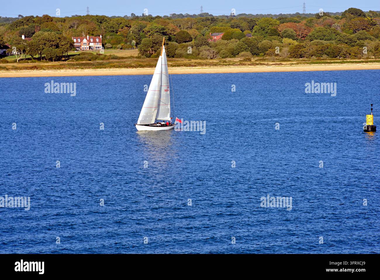 Si vede una barca a vela solitaria entrare nel Southampton Water dal Solent. Una bella proprietà di campagna è visibile sulla riva orientale. Foto Stock