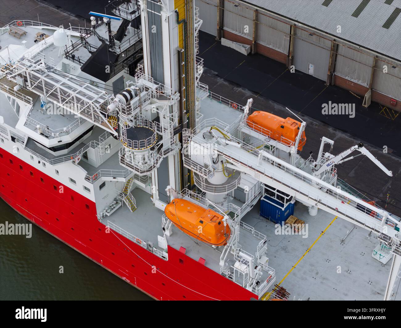 Nave specializzata si prepara per operazioni offshore di energia eolica in un terminal portuale durante il giorno con gru e barche di sicurezza visibili sul ponte Foto Stock