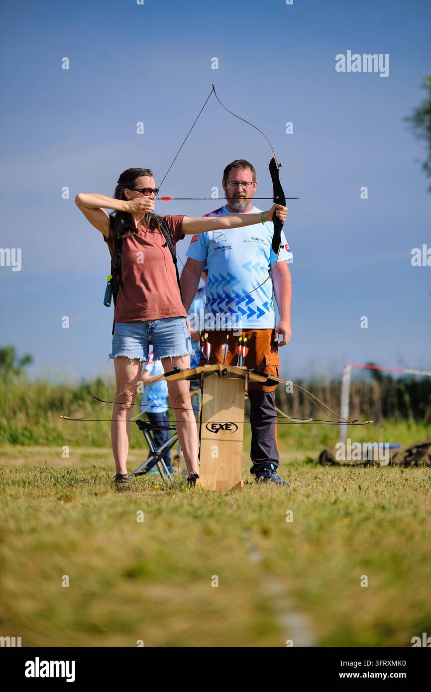 Una donna tende un arco e mira una freccia mentre un uomo le sta accanto durante una pratica di tiro con l'arco all'aperto. Foto Stock