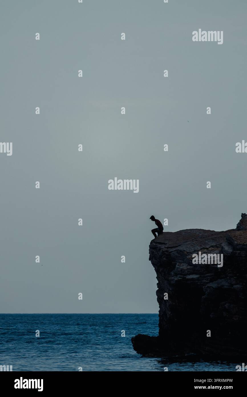 Silhouette di un uomo che si tuffa dall'alta roccia nell'acqua del mare – sport estremo Foto Stock