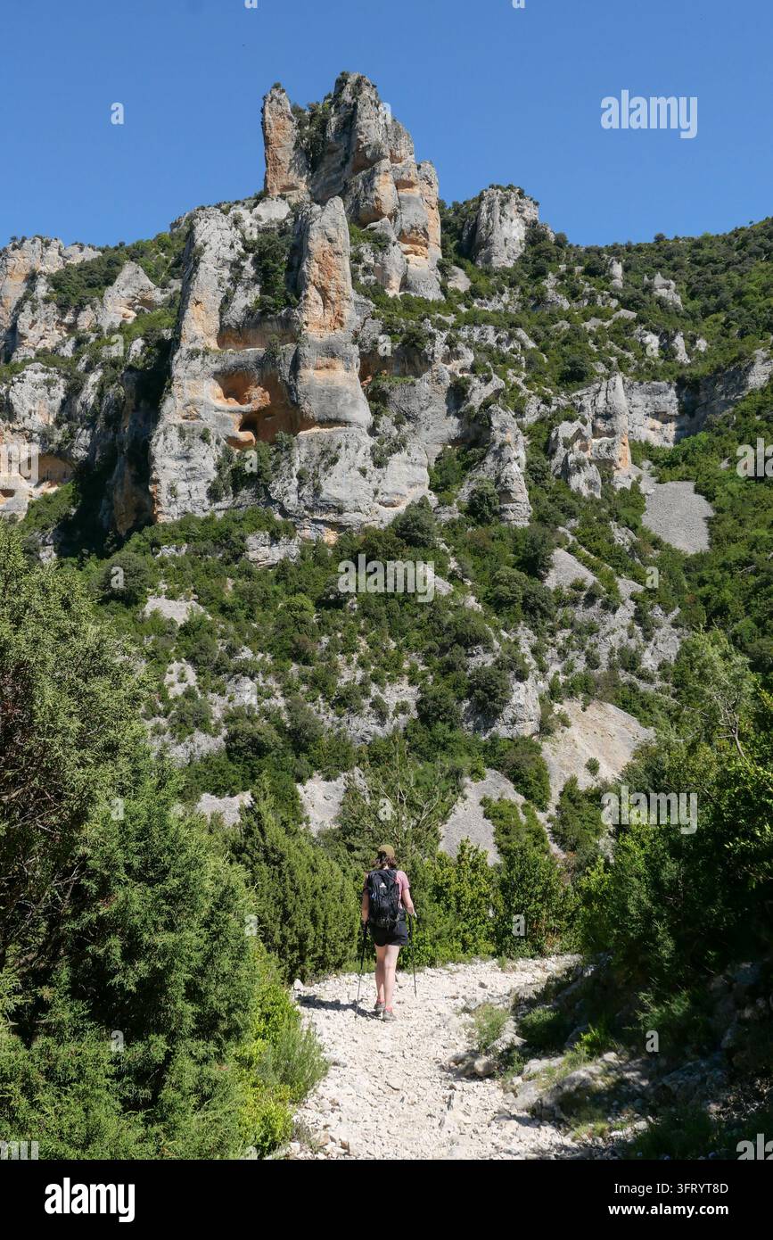 Spagna, Aragona, Provincia di Huesca: escursionista con pantaloncini, cappello e zaino, su un sentiero roccioso sulle alture del canyon di Mascún, nel cuore di Foto Stock