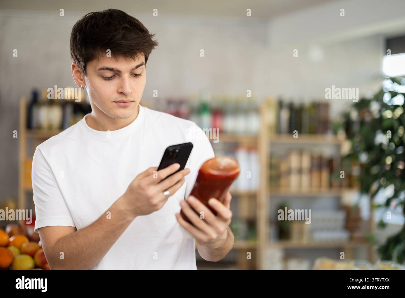 L'acquirente maschio verifica l'idoneità - scansiona il codice QR sul contenitore dell'etichetta ketchup nel negozio di alimentari Foto Stock