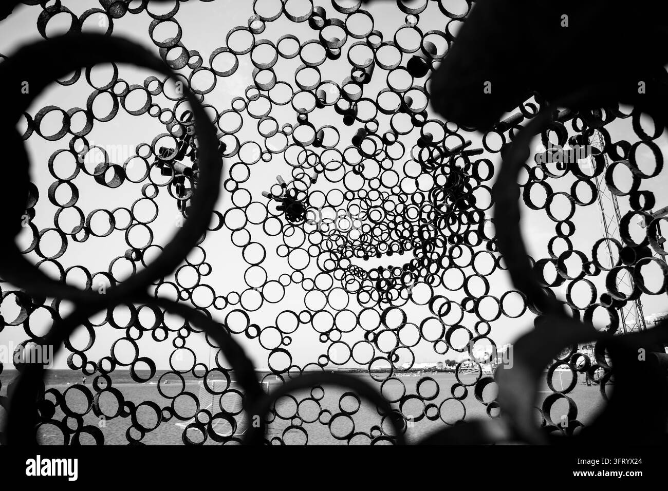 Vista della spiaggia attraverso una scultura in anello di metallo arrugginito con texture a motivo circolare. Bianco e nero. Foto Stock