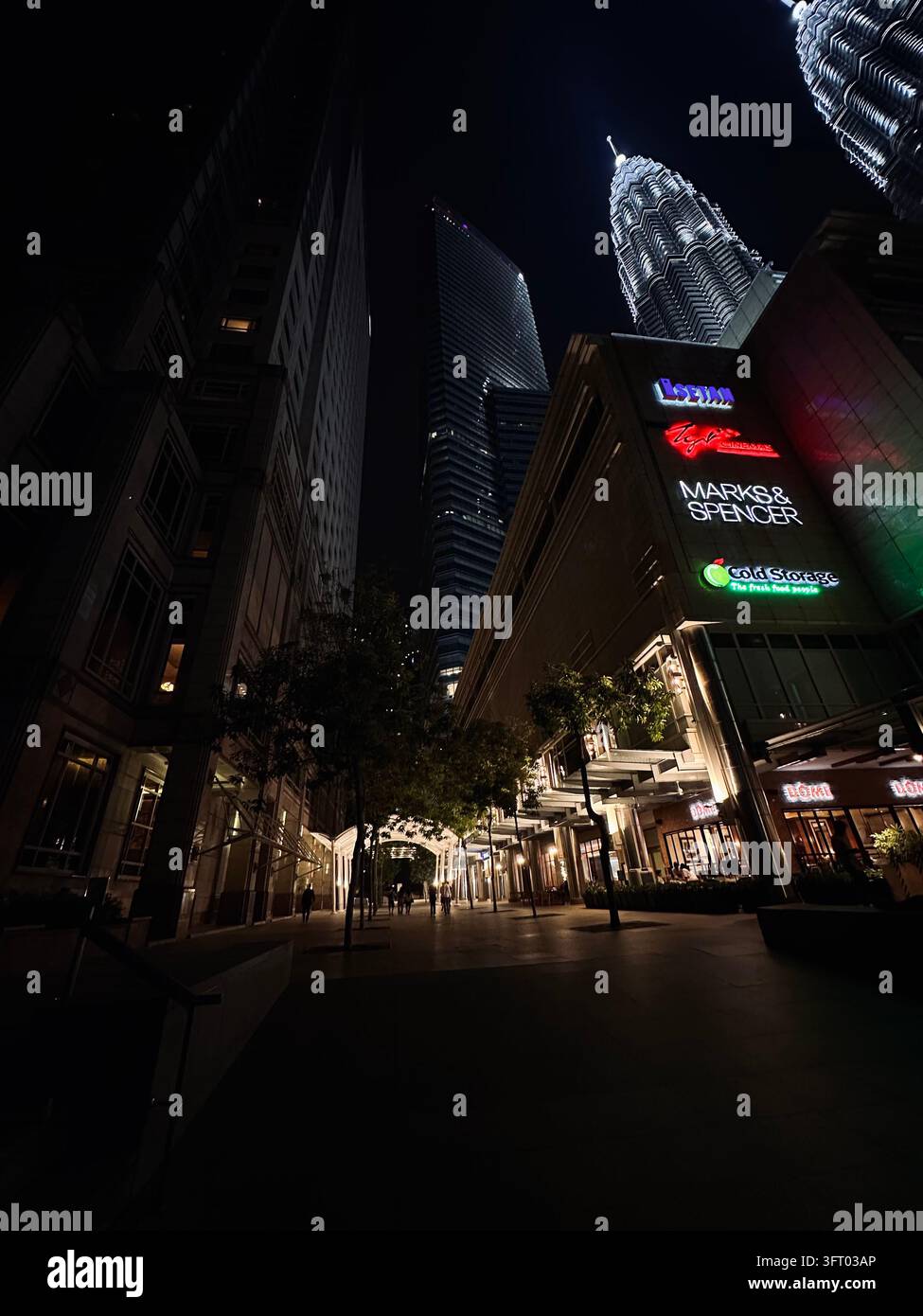 Insegne luminose di negozi delimitano un passaggio pedonale a Kuala Lumpur sotto imponenti edifici di notte. - Immagine stock catturata con smartphone