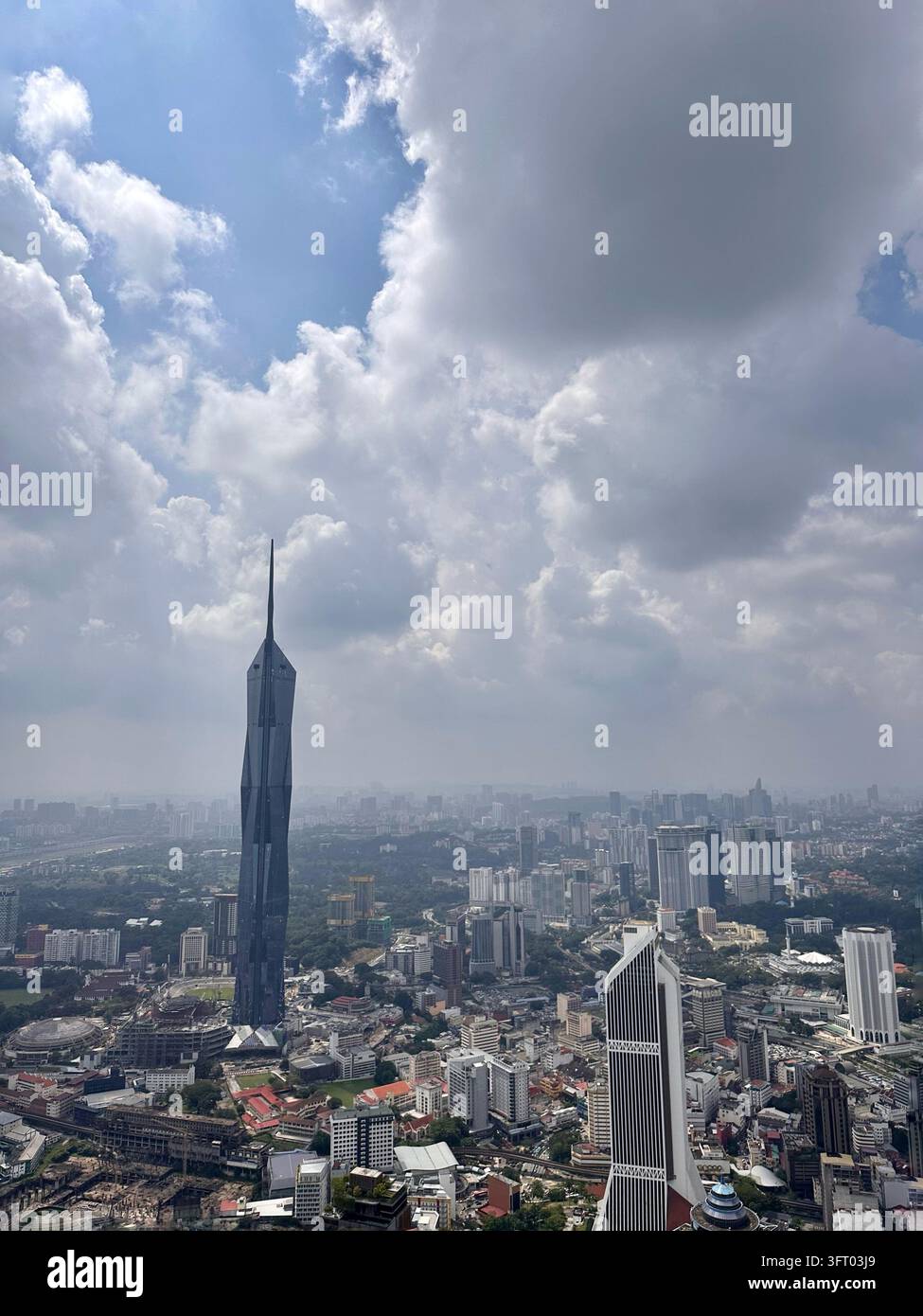 Kuala Lumpur, Malesia - 27 novembre 2022:     Un grattacielo angolare si erge sopra un vasto panorama urbano sotto grandi nuvole in una luce diurna nebbiosa. Foto Stock
