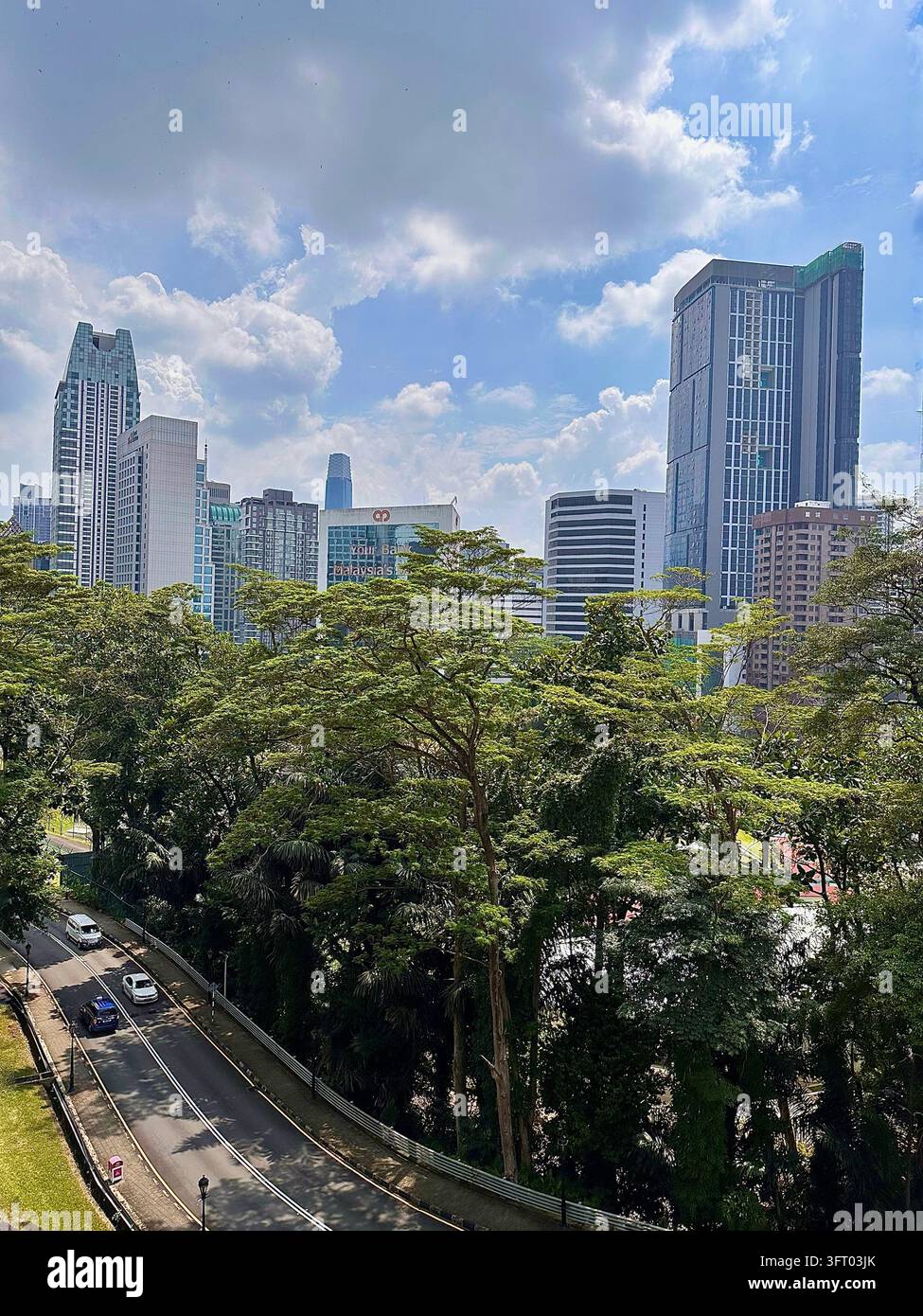 Kuala Lumpur, Malesia - 27 novembre 2022: torri di città moderna si ergono sopra alberi tropicali fitti e traffico alla luce del giorno. - Immagine stock catturata con smartphone