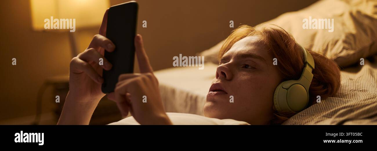 Adolescente con cuffie che usa lo smartphone mentre è sdraiato a letto di notte Foto Stock