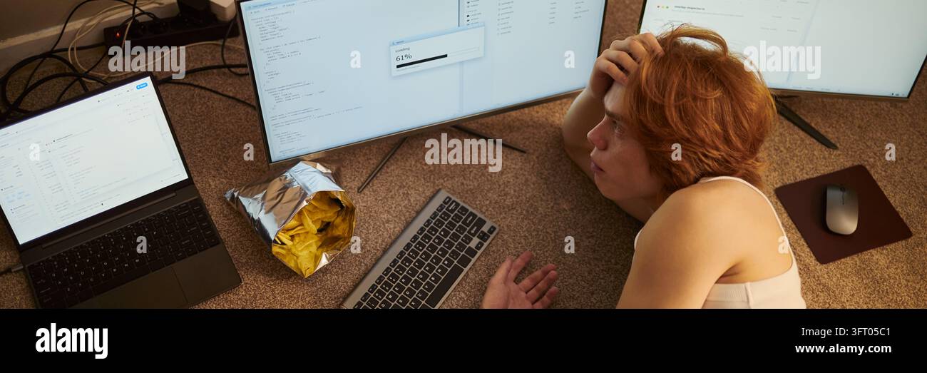 Uomo che programma software e attende il download dei dati sul pavimento Foto Stock