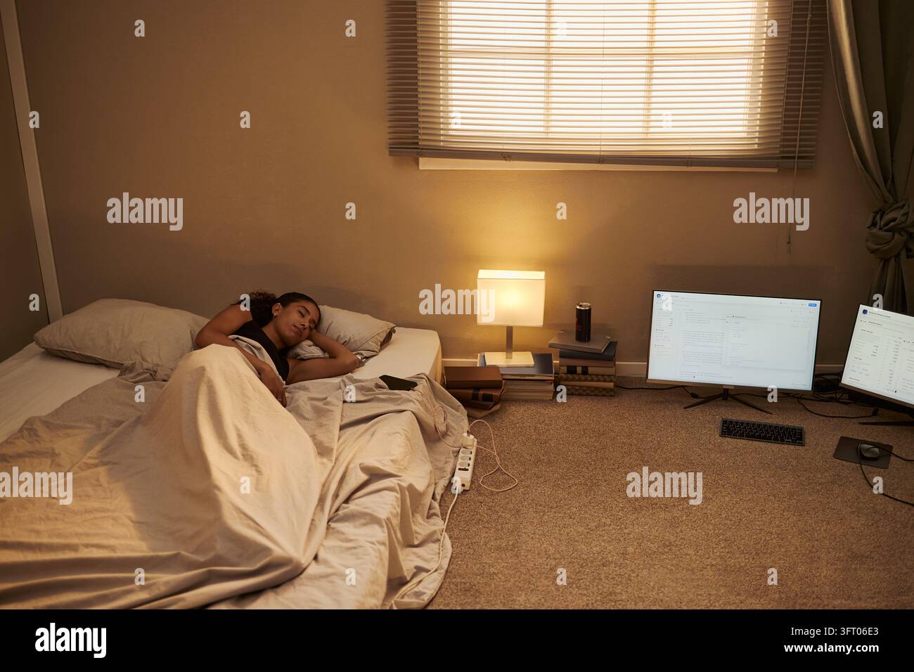 Donna nera che dorme in una camera da letto spoglia vicino a monitor di computer Foto Stock
