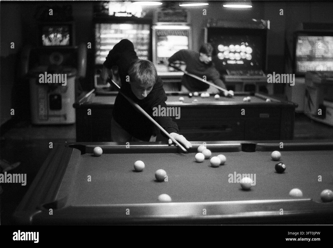 Giocatore chinato su un tavolo da biliardo in una sala giochi, con macchinette da gioco sullo sfondo. Castlebar, Contea di Mayo, Irlanda. 2000 Foto Stock