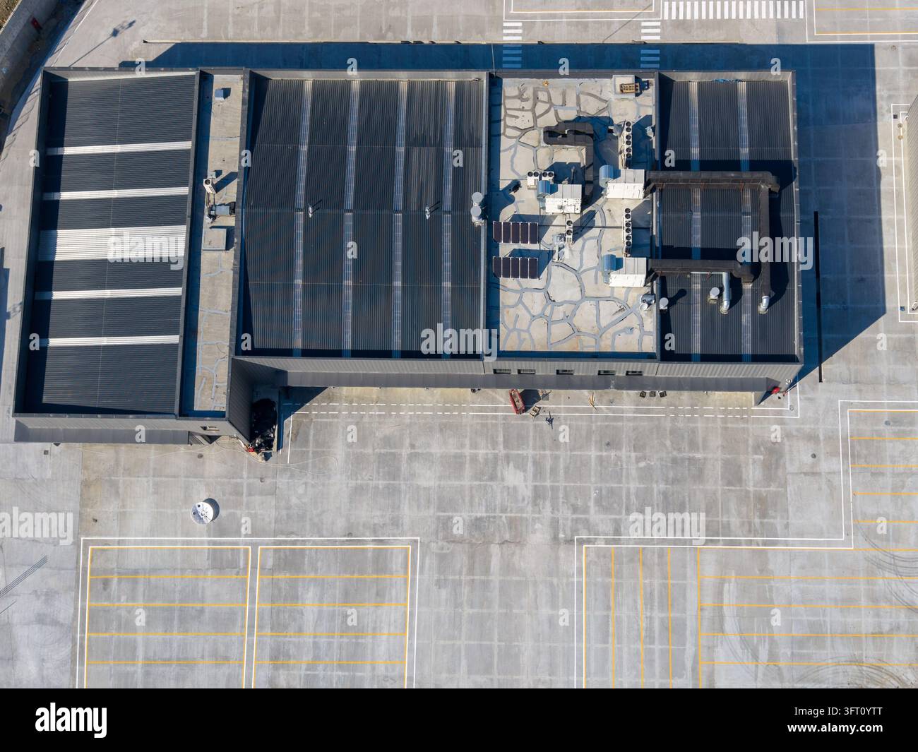 Veduta aerea di un tetto di edificio industriale moderno con unità HVAC e pannelli solari, accanto a un parcheggio in cemento con segnaletica gialla a Istanbul Foto Stock