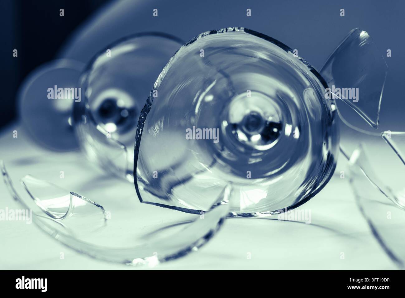 Vetro di vino rotto circondato da frammenti sparsi con toni blu freddi, che illustrano crisi, interruzione, ripresa, resilienza e superamento delle avversità Foto Stock