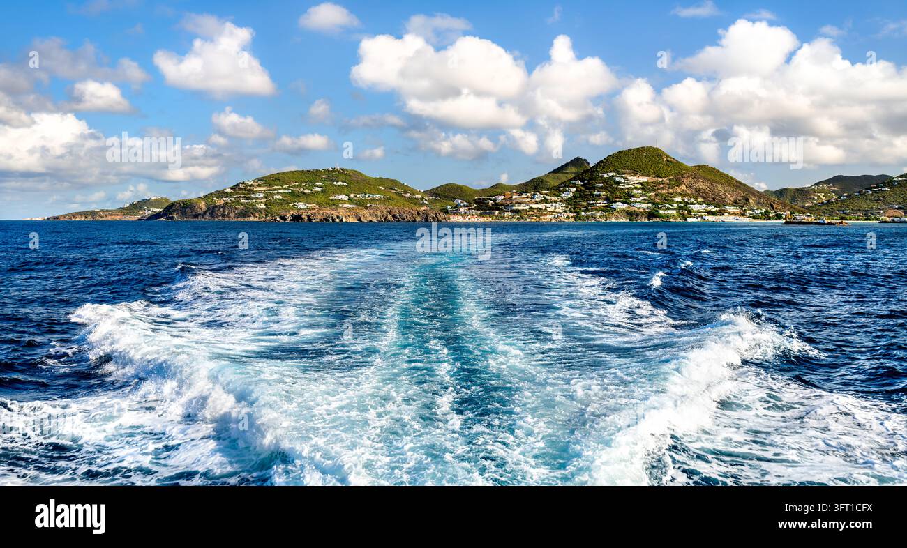 Vista scenica sull'oceano delle rigogliose colline verdi e della costa dell'isola di Sint Maarten, vista dal risucchio turbolento di una barca Foto Stock