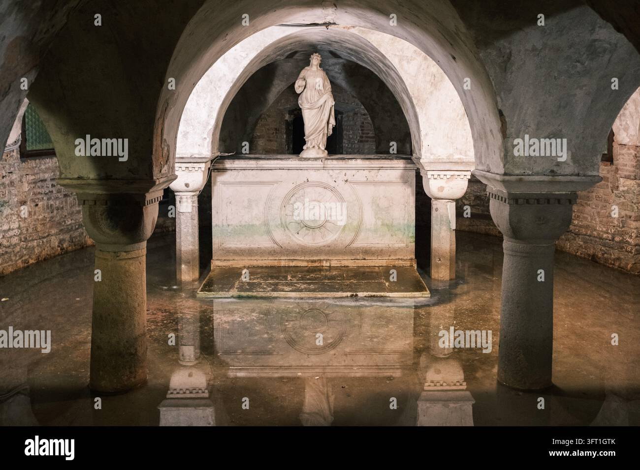 Vista della cripta allagata della Chiesa di San Zaccaria con antiche colonne di pietra, soffitti a volta e una statua di marmo riflessa nell'acqua ferma Foto Stock