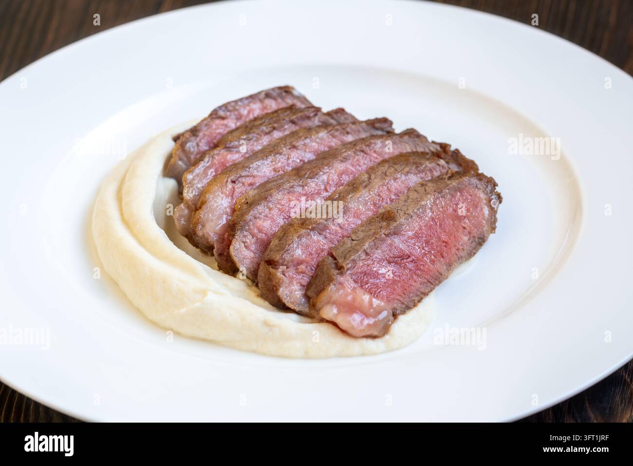 Teneri fette di Wagyu a cottura media rare si adagiano su una vellutata purea di sedano rapa in un'elegante presentazione da ristorante. Foto Stock