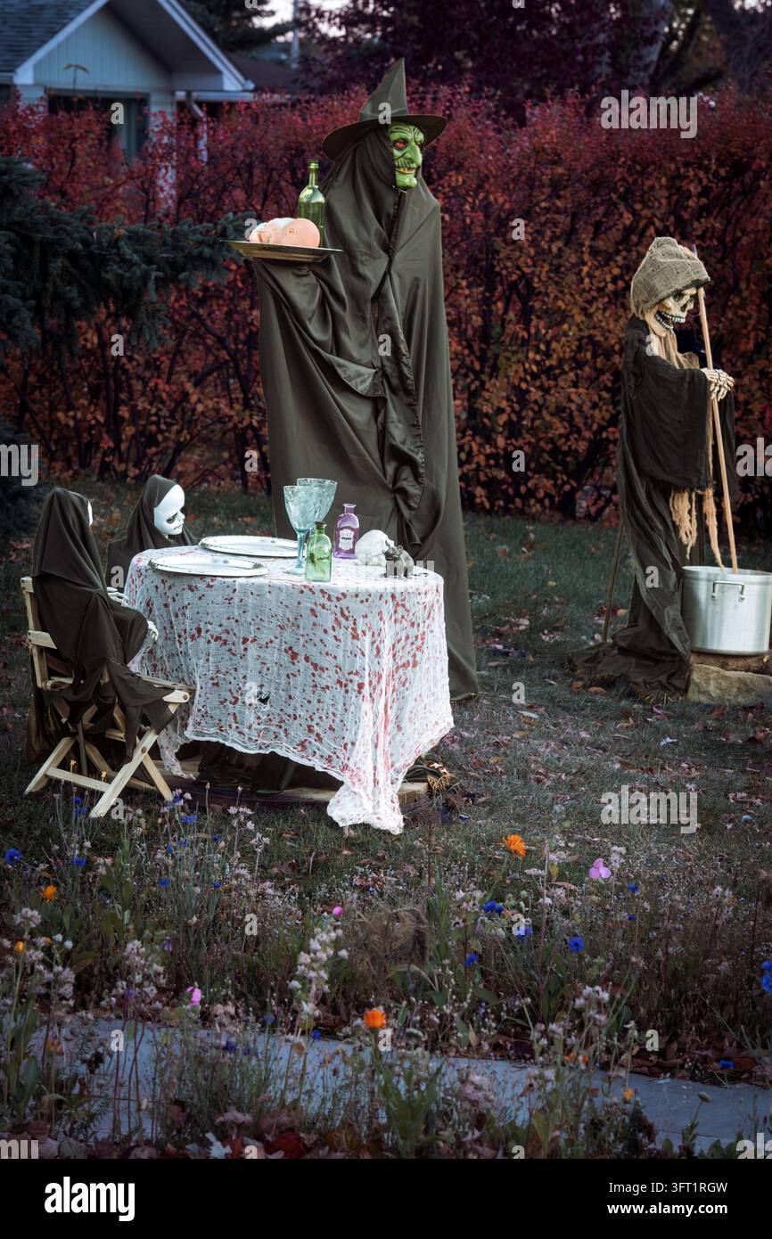Esposizione per una cena all'aperto a tema Halloween con due figure di ghoul vestite con abiti neri, una tovaglia macchiata di sangue, bicchieri in stile vintage Foto Stock
