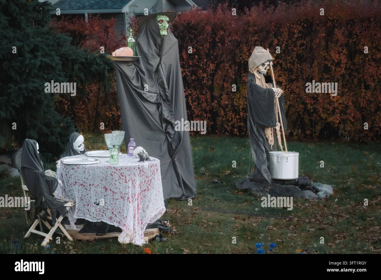 Esposizione per una cena all'aperto a tema Halloween con due figure di ghoul vestite con abiti neri, una tovaglia macchiata di sangue, bicchieri in stile vintage Foto Stock