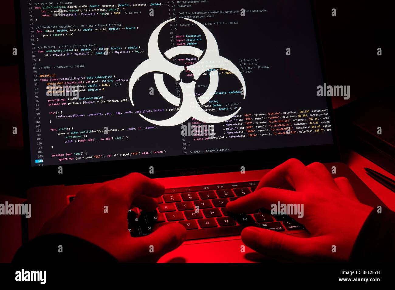Simbolo di biohazard sopra il codice sullo schermo del laptop mentre un hacker digita alla luce rossa Foto Stock