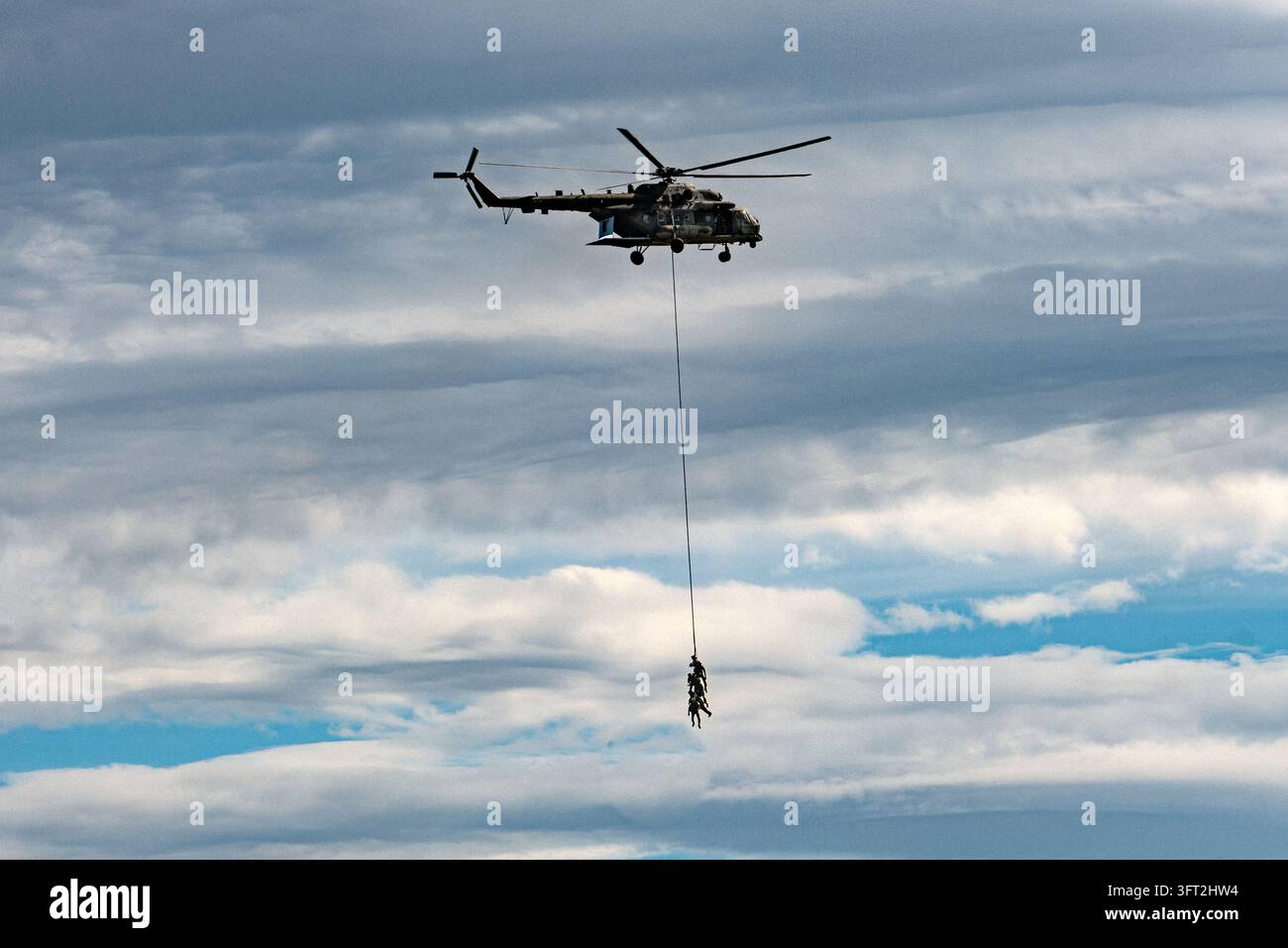 Elicottero da trasporto militare che si libra in un cielo nuvoloso mentre i soldati vengono calati su una lunga corda durante un'esercitazione di addestramento aereo scena 1 Foto Stock